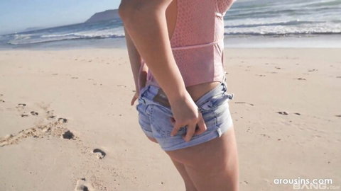Rebecca Volpetti in pink crop top and denim shorts on sunny beach