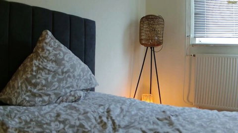 Cozy empty bedroom with gray pillows on black headboard and glowing wicker lamp ready for naughty solo play