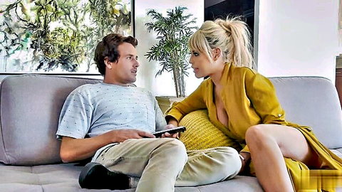 Blonde with huge tits in low-cut yellow dress leaning seductively toward man on couch