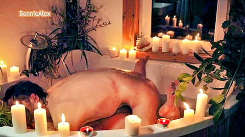 Nude man in romantic candlelit bathtub, rear view