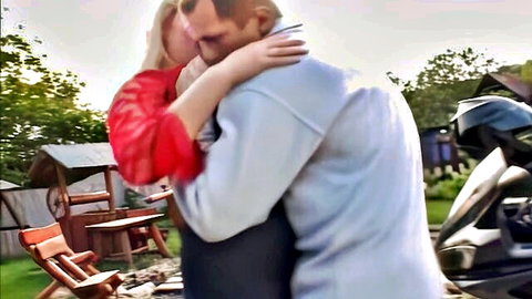 Blonde in sheer red top hugs guy from behind outdoors near motorcycle
