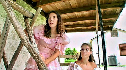 Two sexy women in frilly pink and white dresses, brunette climbing wooden ladder outdoors with blonde watching