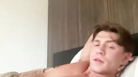 Handsome shirtless young man lying on bed with mouth agape moaning in pleasure