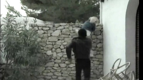 Blonde woman lifted by man against stone wall in classic outdoor scene