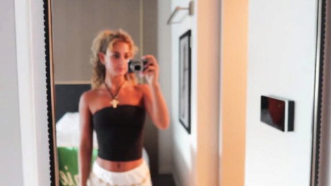 Blonde model mirror selfie in black tube top and white shorts at fashion week