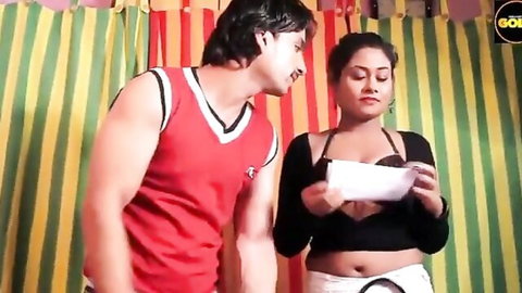 Indian couple in teasing pose, man in red tank top leans toward curvy woman in black top and white skirt showing cleavage