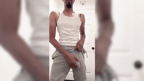 Sexy ebony guy in gray sweatpants teasing bulge in tank top