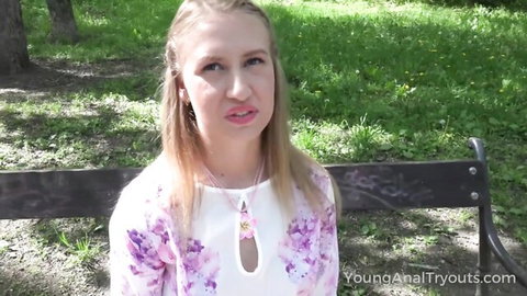 Young blonde teen in floral dress sitting on park bench outdoors teasing