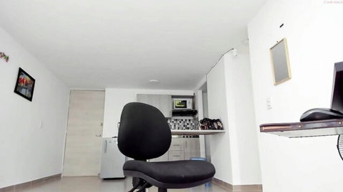 Empty black office chair facing kitchenette with fridge, microwave, and computer desk in small apartment room