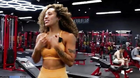 Curly-haired biracial fitness model in orange gymwear poses during workout