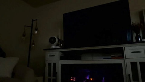 Cozy dimly lit living room setup with TV, electric fireplace, fan and ambient purple lights for webcam tease