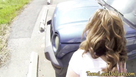 Blonde teen in tight white tank top leaning over blue SUV outdoors amateur style