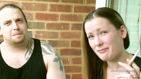 Tattooed man and brunette girlfriend smoking intimately outdoors