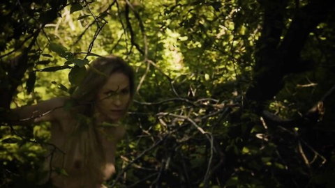 Naked blonde with medium tits poses seductively amid forest branches