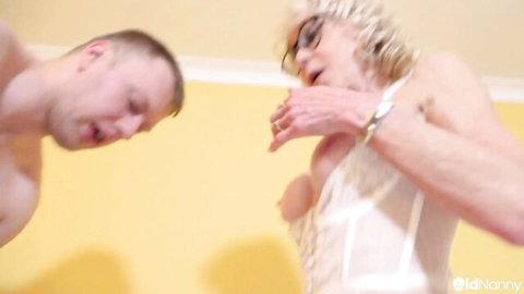 Mature blonde in white lingerie with young shirtless guy in intimate embrace