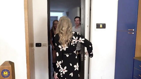 Blonde mature in floral dress seduces young man with another blonde at kitchen doorway threesome tease