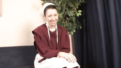 Petite brunette in Amish prayer cap and maroon dress smiling playfully on couch