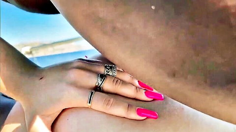 Woman with pink nails and silver rings gripping smooth tanned thighs outdoors