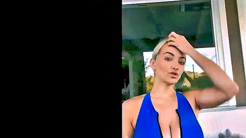 Blonde babe with huge tits cleavage in tight blue halter dress posing seductively by window