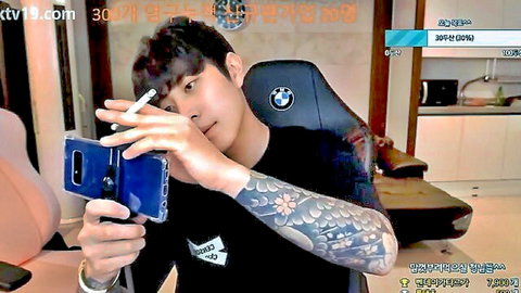 Hot tattooed Korean guy smoking cigarette while taking selfie in BMW gaming chair