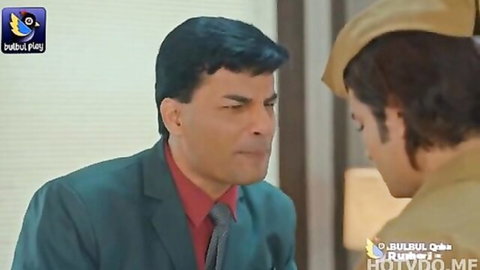 Stern Indian man in green suit confronts younger man in beige uniform intensely