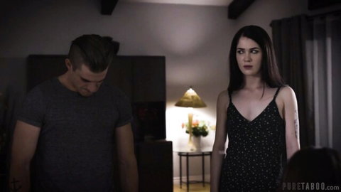 Brunette MILF in black slip dress confronts young stepson in tense taboo bedroom stare-down