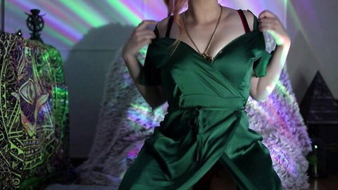 Redhead in shiny green dress teases deep cleavage with mystical background