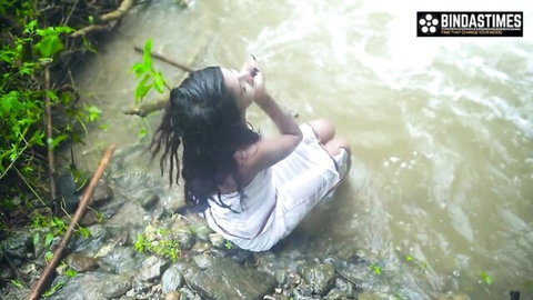 Desi girl in wet white dress drinking at outdoor waterfall