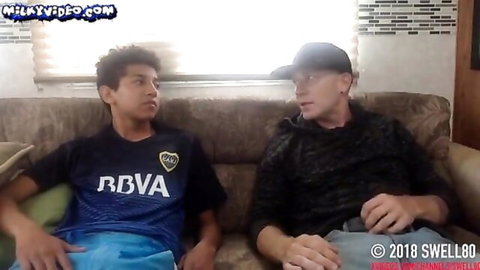 Mature man and young Latino guy in casual clothes on couch, teasing gay encounter