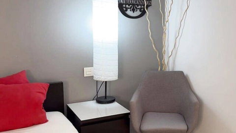 Empty modern bedroom corner with gray walls red pillows white lamp and armchair