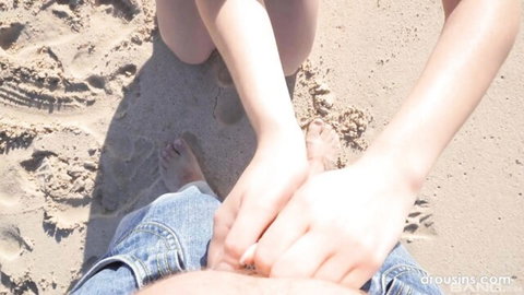 Blonde babe kneels on beach sand gripping thick hard cock from open jeans