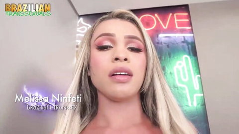Blonde Brazilian transsexual Melissa Ninfeta teases with glossy open lips and deep cleavage