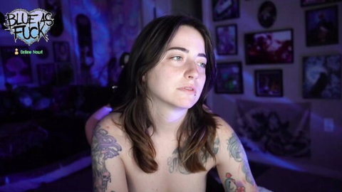 Tattooed brunette lying topless exposing her perky tits on blue-lit webcam show