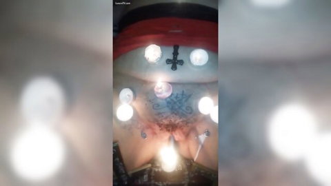 Tattooed woman burning pubic hair in ritual with flames and inverted cross