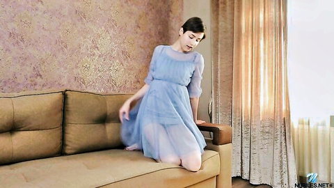 Virginia in sheer blue dress kneeling on sofa, solo tease