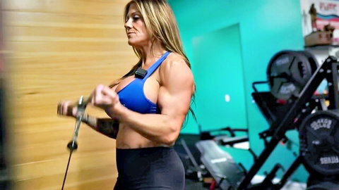 Muscular blonde woman flexing biceps in tight sports bra during gym workout