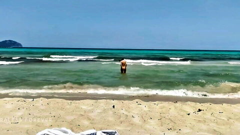Blonde Ellie standing topless in nudist beach waters