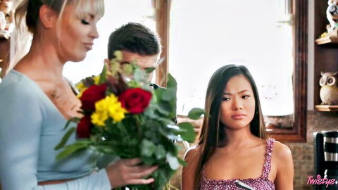 Busty blonde hands roses to petite Asian beauty while guy watches intently