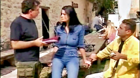 Brunette in tight denim outfit talks with two men in outdoor adult scene
