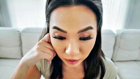 Seductive Asian beauty with heavy glam makeup and glossy lips smiling closeup on couch