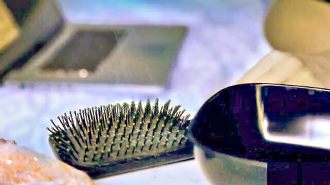 Close-up of black hairbrush over black bowl on bed with laptop and crystals