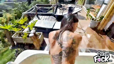 Tattooed wet-haired babe steps into outdoor bathtub nude from behind showing sexy tattooed back and ass