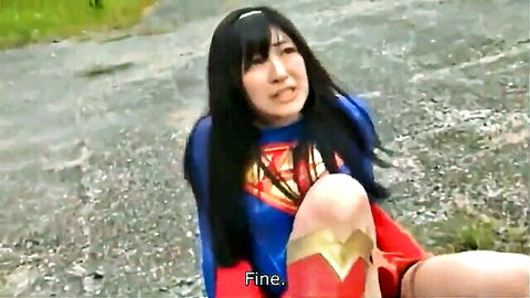 Asian woman in Supergirl cosplay kneeling outdoors with surprised expression