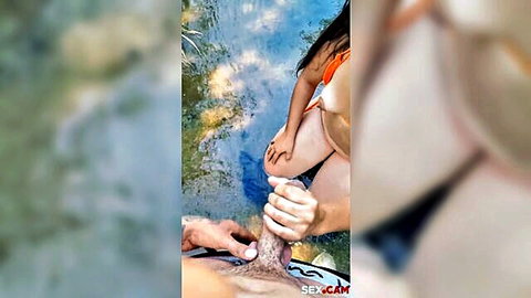 Asian woman in orange bikini gives outdoor blowjob by the water