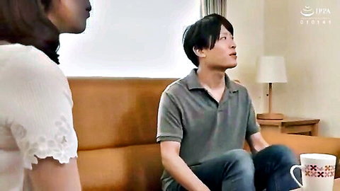 Japanese MILF in lace blouse eyes young man's crotch while he sits on couch holding mug