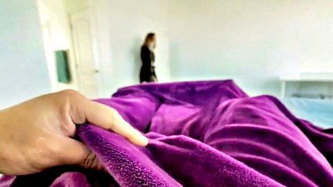Man's hand gripping purple fluffy blankets on bed with woman in black dress in background