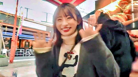 Cute smiling Japanese girl in gray coat making peace signs on urban street