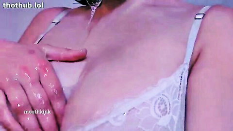 Asian woman in white lace bra with hands squeezing breasts and dripping liquid in mouth kink scene
