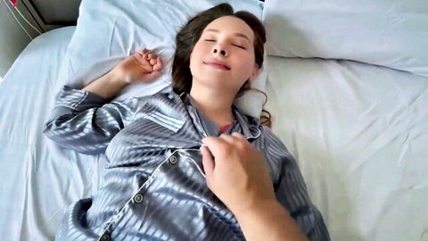 Asian woman in silk pajamas relaxing on bed as partner touches her chest in amateur couple foreplay