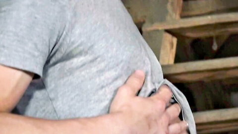 Muscular straight guy in gray t-shirt playfully gripping fabric in attic scene